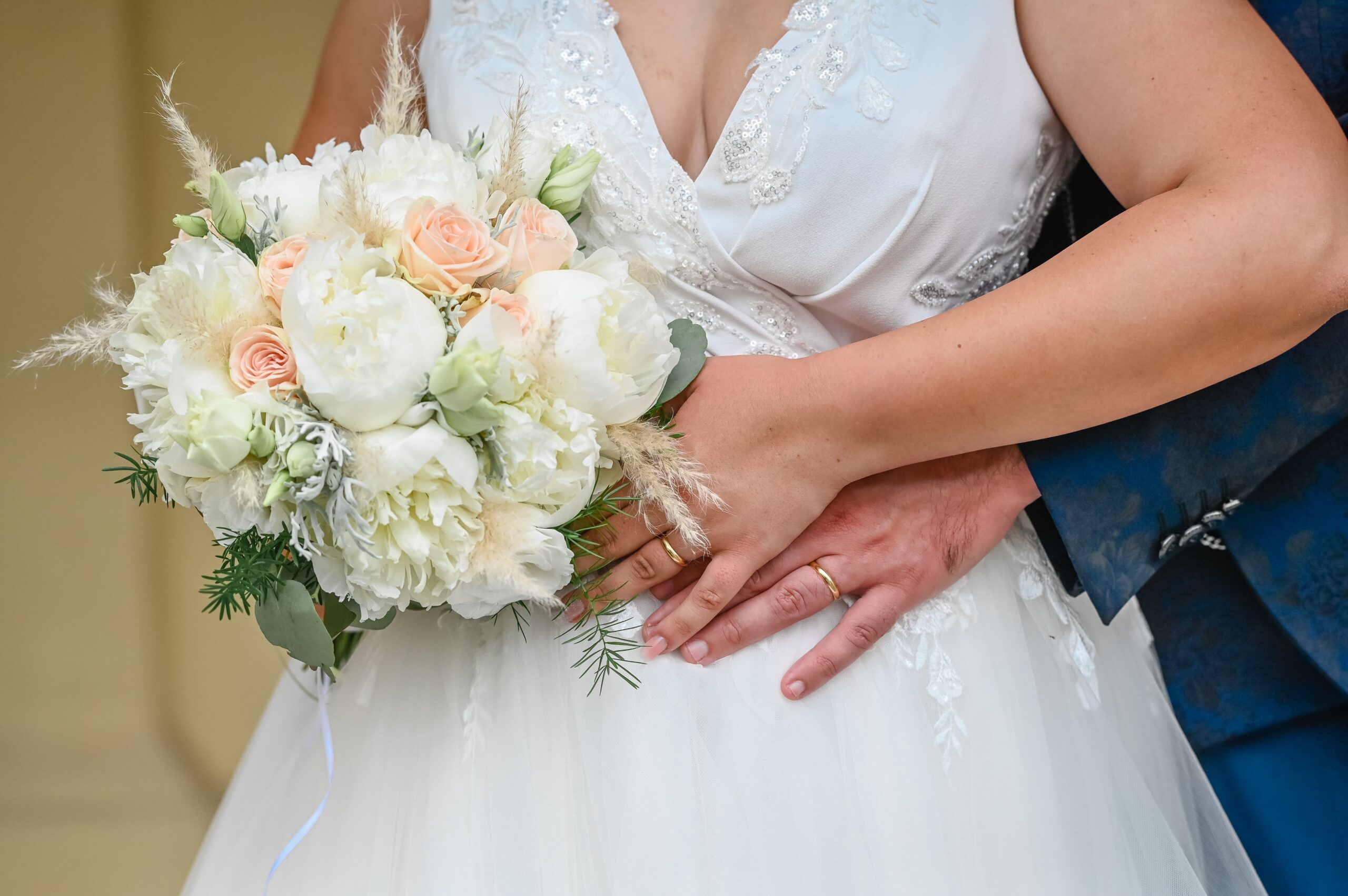 Close-up of bride and groom with elegant bouquet, showcasing wedding rings in an intimate pose.